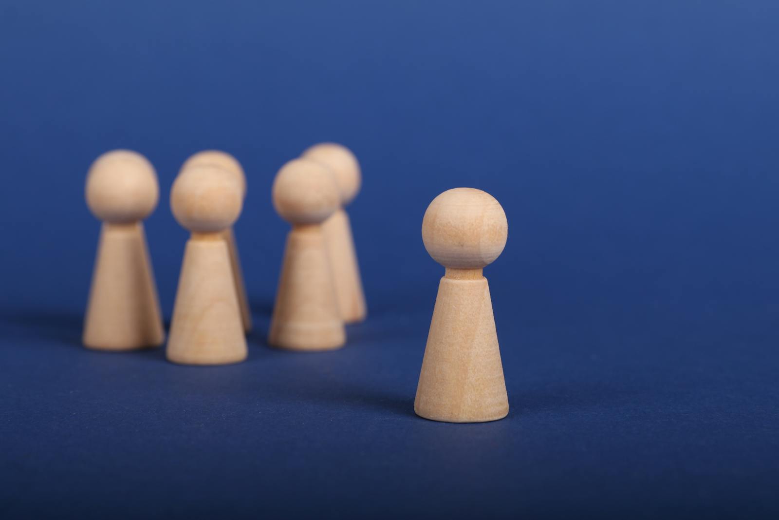 Photo by Ann H Wooden figures on a blue background depicting a leadership concept with one figure leading a group.